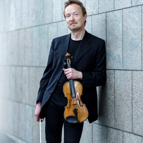 Patrick Sepec mit Geige vor grauer Wand