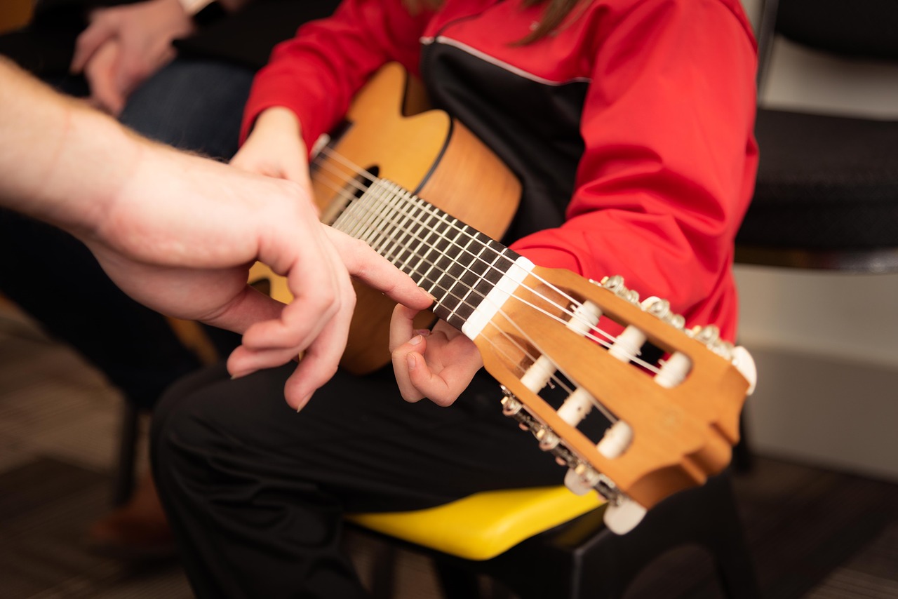 Ein Gitarrenlehrer erklärt seinem Gitarrenschüler die Griffe am Hals der Gitarre.
