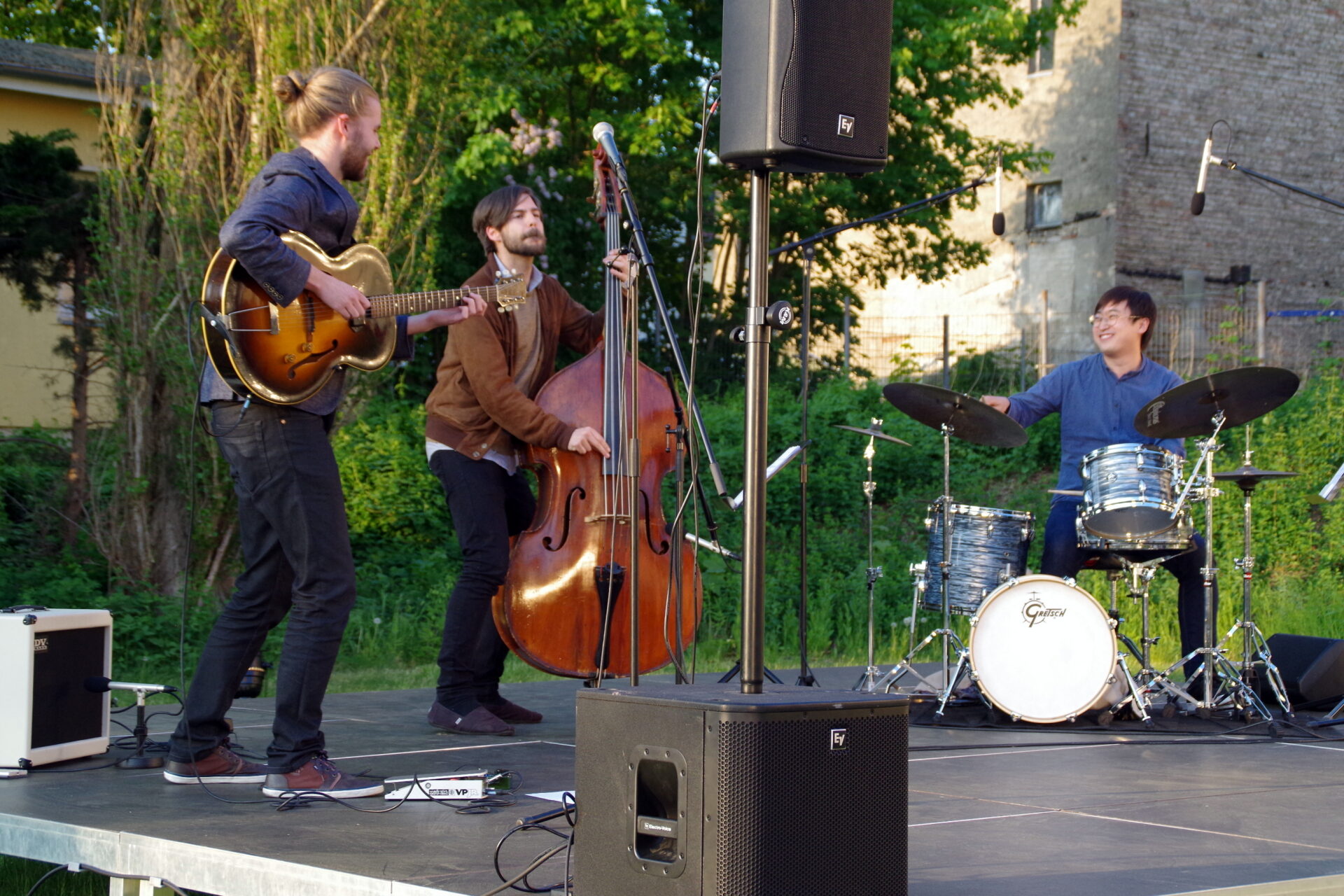 Ein Jazztrio spielt im Freien mit E-Gitarre, Kontrabass und Schlagzeug.